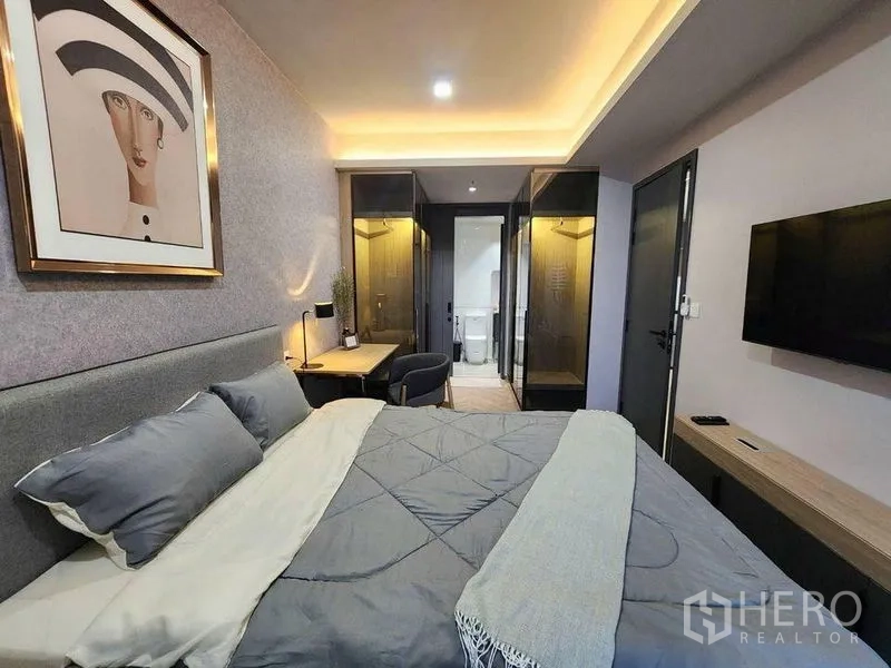 Condominium for rent in Bang Rak, Bangkok - Cozy bedroom with upholstered bed, desk and glass wardrobes leading to the bathroom.