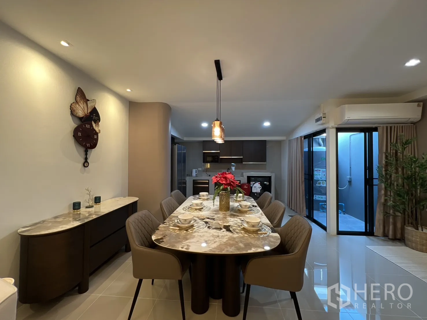 Townhouse for rent in Bang Phli, Samut Prakan - Dining room with a long marble table, decorative wall clock and dual sliding glass doors.