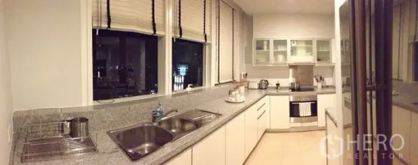 公寓 出租在Ratchathewi, Bangkok - 长廊式厨房，石材台面、双水槽、嵌入式烤箱与窗外城市夜景。