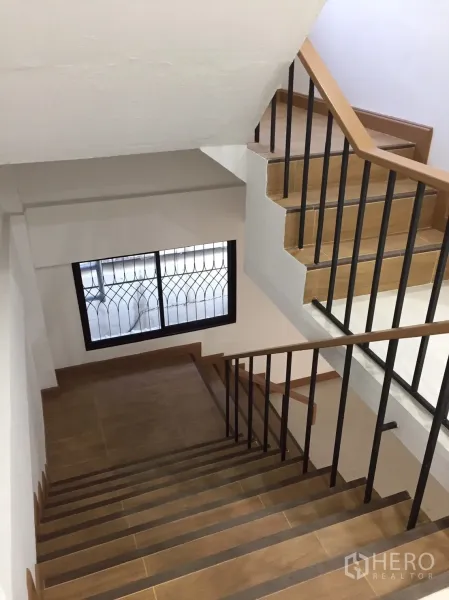 店屋 出租在Suan Luang, Bangkok - 楼梯采用木纹踏步与黑色金属扶手，并配有带护栏的窗户。