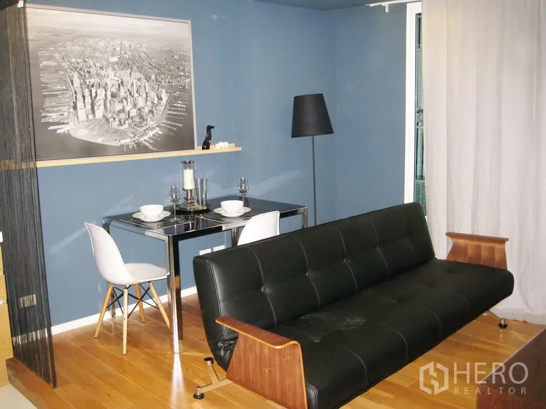 公寓 出租或出售在Bang Rak, Bangkok - 蓝色墙面客厅，黑色皮沙发、双人餐桌与木地板。