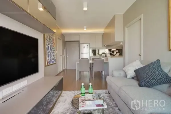 Condominium for rent in Phra Khanong, Bangkok - Bright living room with TV wall, grey sofa and open-plan dining to modern kitchen.