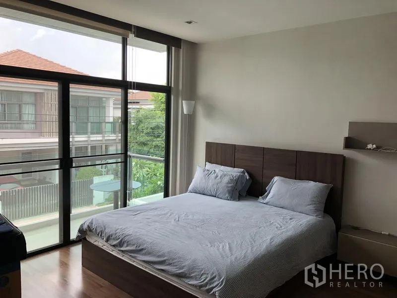 Detached House for rent in Bang Kapi, Bangkok - Master bedroom with wood flooring, king bed, and full-height glass wall to a balcony.