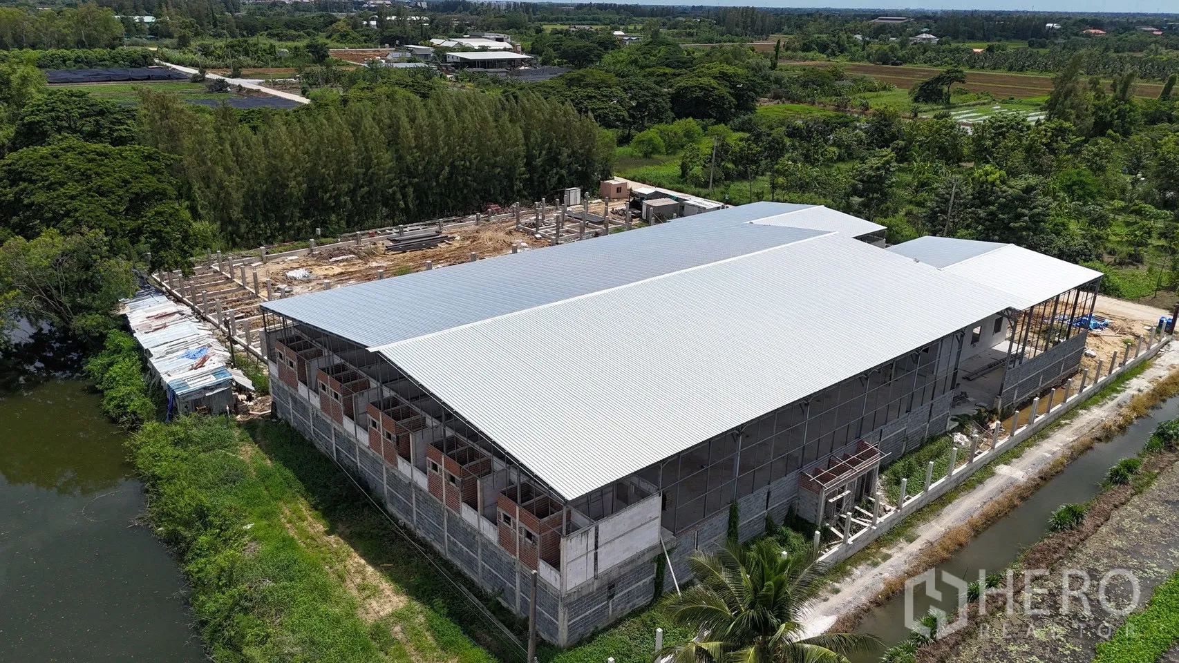 Factory for rent in Phutthamonthon, Nakhon Pathom - Rear aerial of long factory building bordering a canal and vegetation.