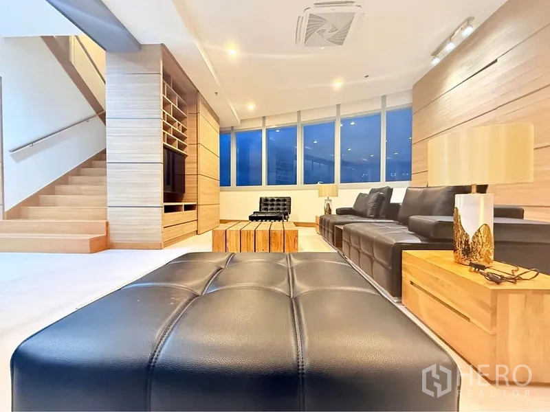 คอนโด ให้เช่าหรือขายในKhlong Toei, Bangkok - มุมต่ำของห้องนั่งเล่น มีออตโตมัน โต๊ะข้างโคมไฟ ผนังทีวีบิวท์อินและบันได