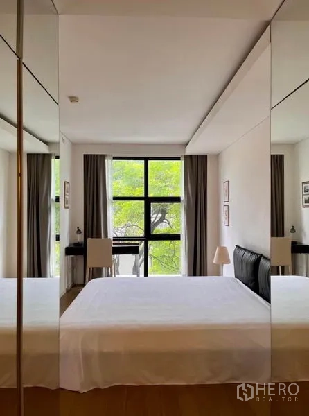 Condominium for rent in Watthana, Bangkok - Serene bedroom with a large black-framed window offering garden views.
