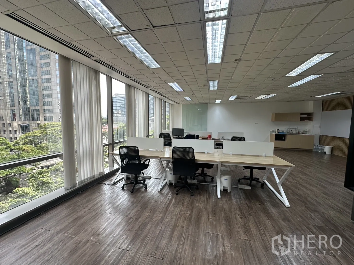 Office Space for rent - Open workspace with city views, vertical blinds, and a kitchenette at the far end.