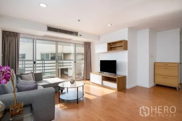 公寓 出租在Khlong Toei, Bangkok - 明亮客厅，灰色沙发、电视柜，落地推拉门通向阳台，木地板。