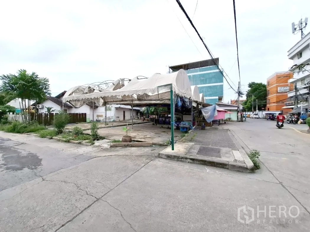 Land for rent in Bang Kapi, Bangkok - Wide view of the open paved plot with arched canopies and surrounding buildings.