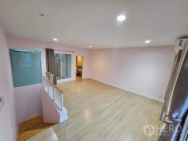 Townhouse for rent in Wang Thonglang, Bangkok - Bright upper-floor family room with wood flooring, railing, and large window with curtains.