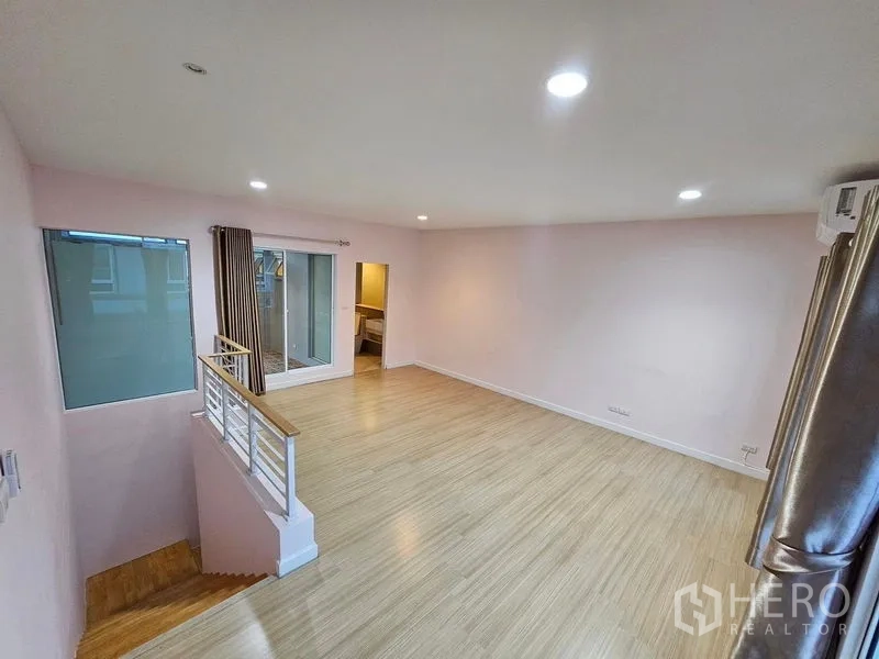 Townhouse for rent in Wang Thonglang, Bangkok - Bright upper-floor family room with wood flooring, railing, and large window with curtains.