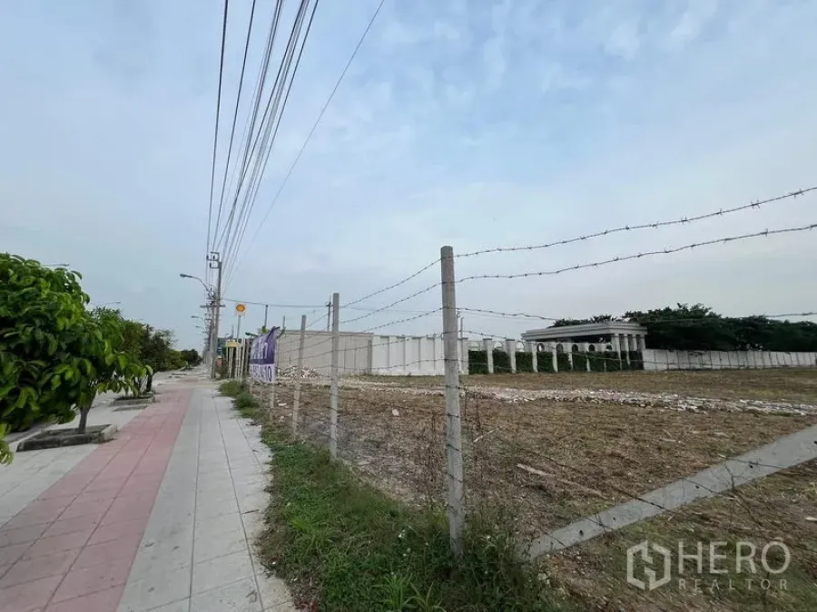ที่ดิน ให้เช่าในLat Krabang, Bangkok - ภาพมุมมองริมถนนของที่ดินล้อมรั้วลวดหนาม มีทางเท้า สายไฟ และอาคารเตี้ยใกล้เคียง