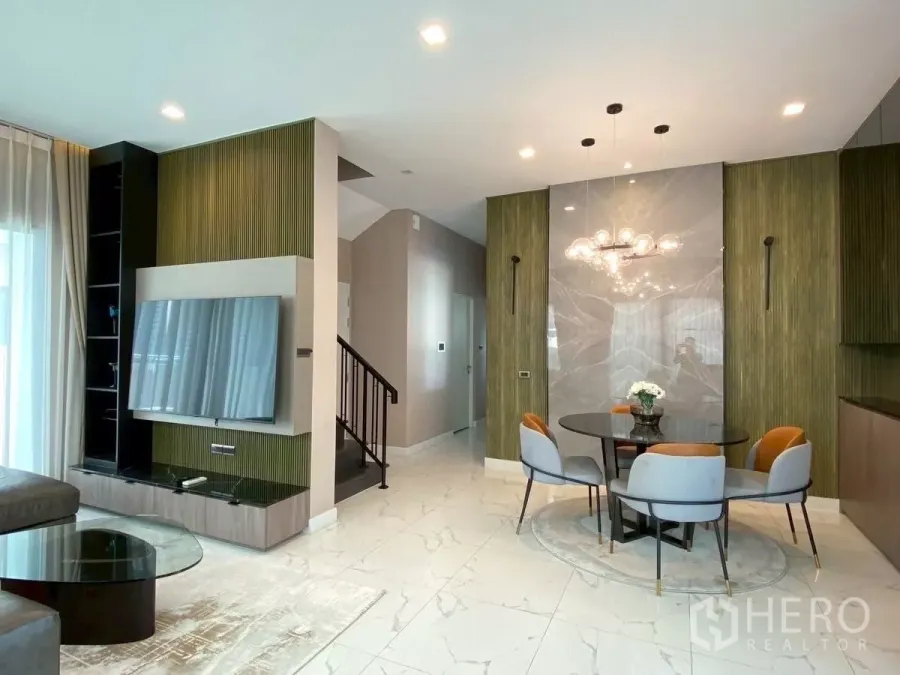 Detached House for rent in Bang Phli, Samut Prakan - Open-plan living and dining area with marble-look floors, feature TV wall and a round table under a modern chandelier.
