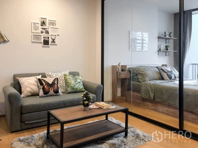 คอนโด ให้เช่าหรือขายในBang Rak, Bangkok - ห้องนั่งเล่นอบอุ่น โซฟาสีเทา โต๊ะกลางไม้ และผนังกระจกเปิดเชื่อมห้องนอน