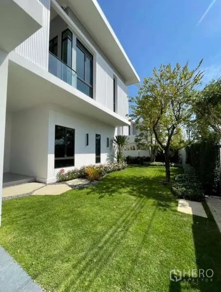 Detached House for rent in Samut Prakan - Landscaped side garden beside modern white two-storey house.