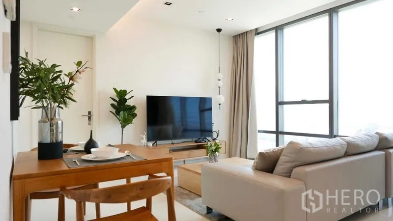 Condominium for rent in Sathon, Bangkok - Bright living room with sofa, TV console, dining set and floor-to-ceiling windows in a Sathorn condo.