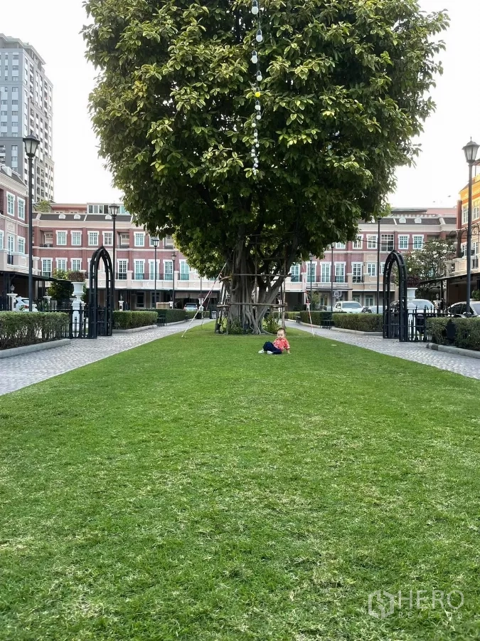 Townhouse for sale in Watthana, Bangkok - Community green lawn with a large shade tree and townhouse blocks beyond.