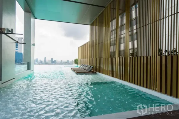 Condominium for rent in Watthana, Bangkok - Infinity-edge swimming pool with sun loungers and panoramic Bangkok skyline outlook.