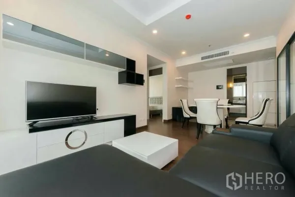 Condominium for rent in Sathon, Bangkok - Open‑plan living and dining area with TV unit and four‑seat dining set leading to a bedroom doorway.
