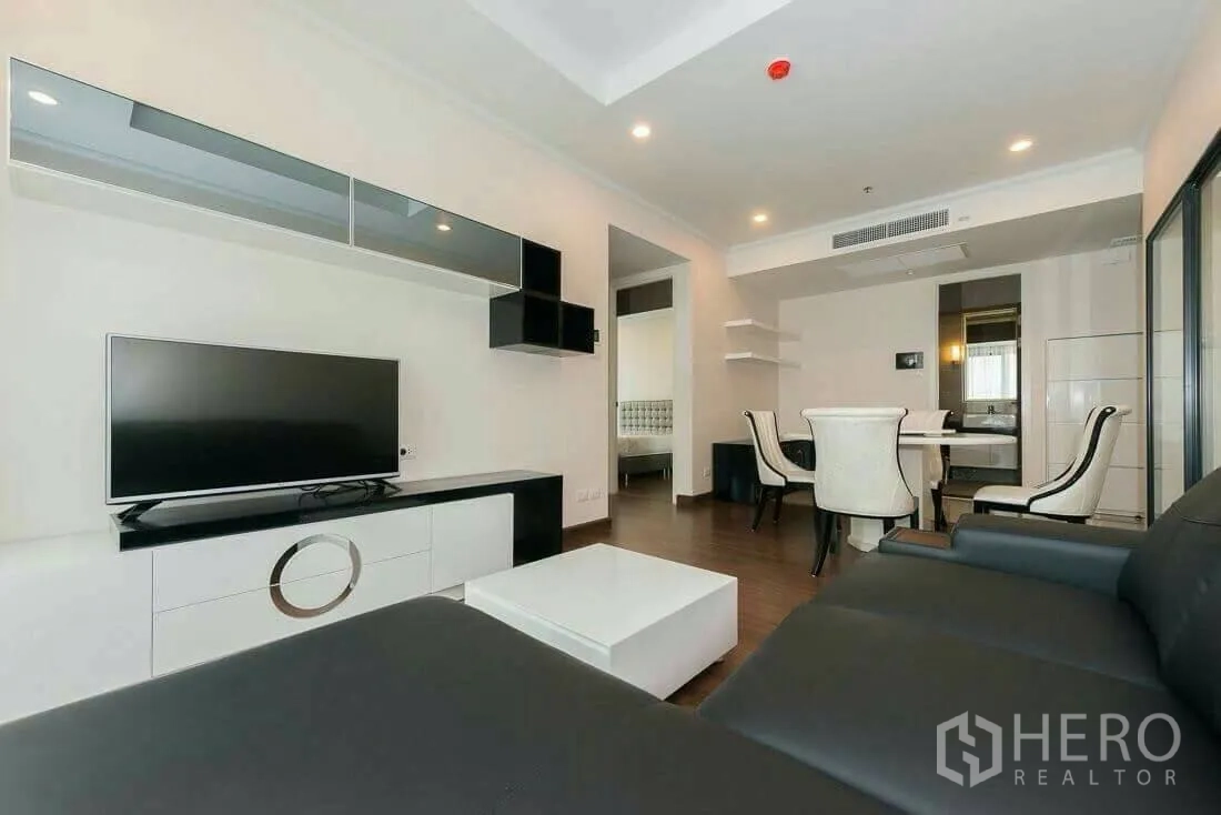 Condominium for rent in Sathon, Bangkok - Open‑plan living and dining area with TV unit and four‑seat dining set leading to a bedroom doorway.