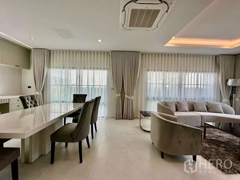 独立式住宅 出租在Bang Phli, Samut Prakan - 采光充足的客餐厅，落地窗纱帘、弧形沙发与大理石餐桌，现代风格。