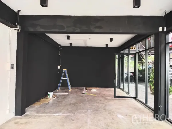 พื้นที่ขายปลีก ให้เช่า - พื้นที่ค้าปลีกผนังสีดำ ไฟเพดาน และประตูกระจกมุมเปิดสู่คอร์ทยาร์ด ระหว่างปรับปรุง