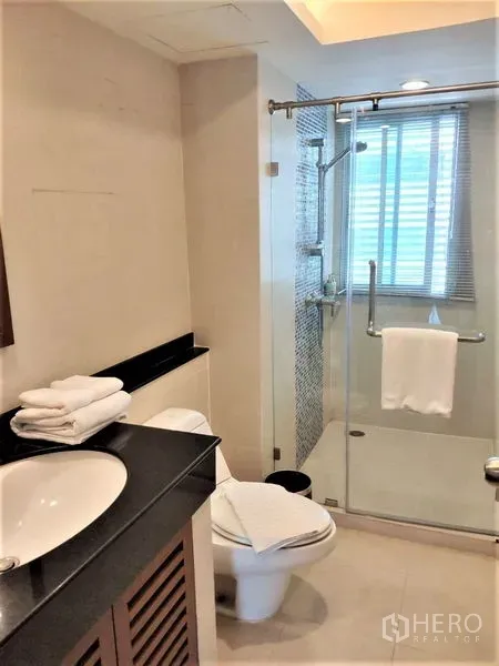 Condominium for rent in Bang Rak, Bangkok - Modern bathroom featuring a glass-enclosed shower, vanity countertop, toilet and window for natural light.