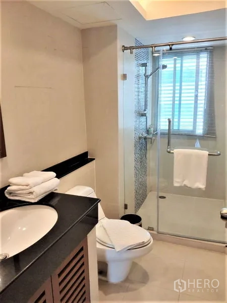 Condominium for rent in Bang Rak, Bangkok - Modern bathroom featuring a glass-enclosed shower, vanity countertop, toilet and window for natural light.