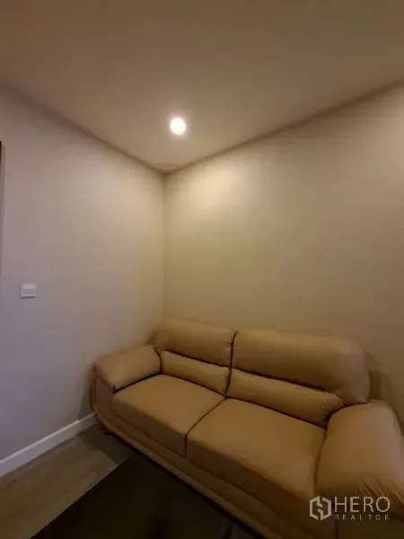 公寓 出租在Bang Rak, Bangkok - 温馨角落，米色皮沙发与筒灯照明。