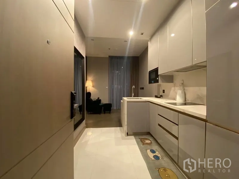 Condominium for rent in Huai Khwang, Bangkok - Entrance view of a sleek galley kitchen opening to a softly lit living area.