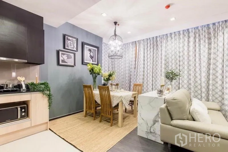 คอนโด ให้เช่าหรือขายในWatthana, Bangkok - มุมทานข้าวโต๊ะไม้พร้อมโคมไฟแขวน ข้างครัวรูปตัวแอลและกรอบภาพตกแต่ง