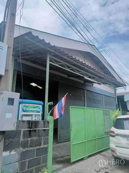 货栈 出售在Khlong Luang, Pathum Thani - 仓库临街外观，绿色大门与多扇卷闸门，前方可停车
