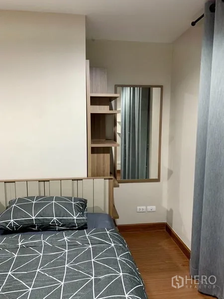 Condominium for rent in Huai Khwang, Bangkok - Bedroom corner showing bed, built-in shelving and a full-length mirror beside grey curtains.