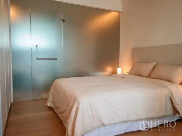 Condominium for rent in Watthana, Bangkok - Cozy bedroom with double bed, soft lighting, hardwood floor, and frosted glass partition to the ensuite.