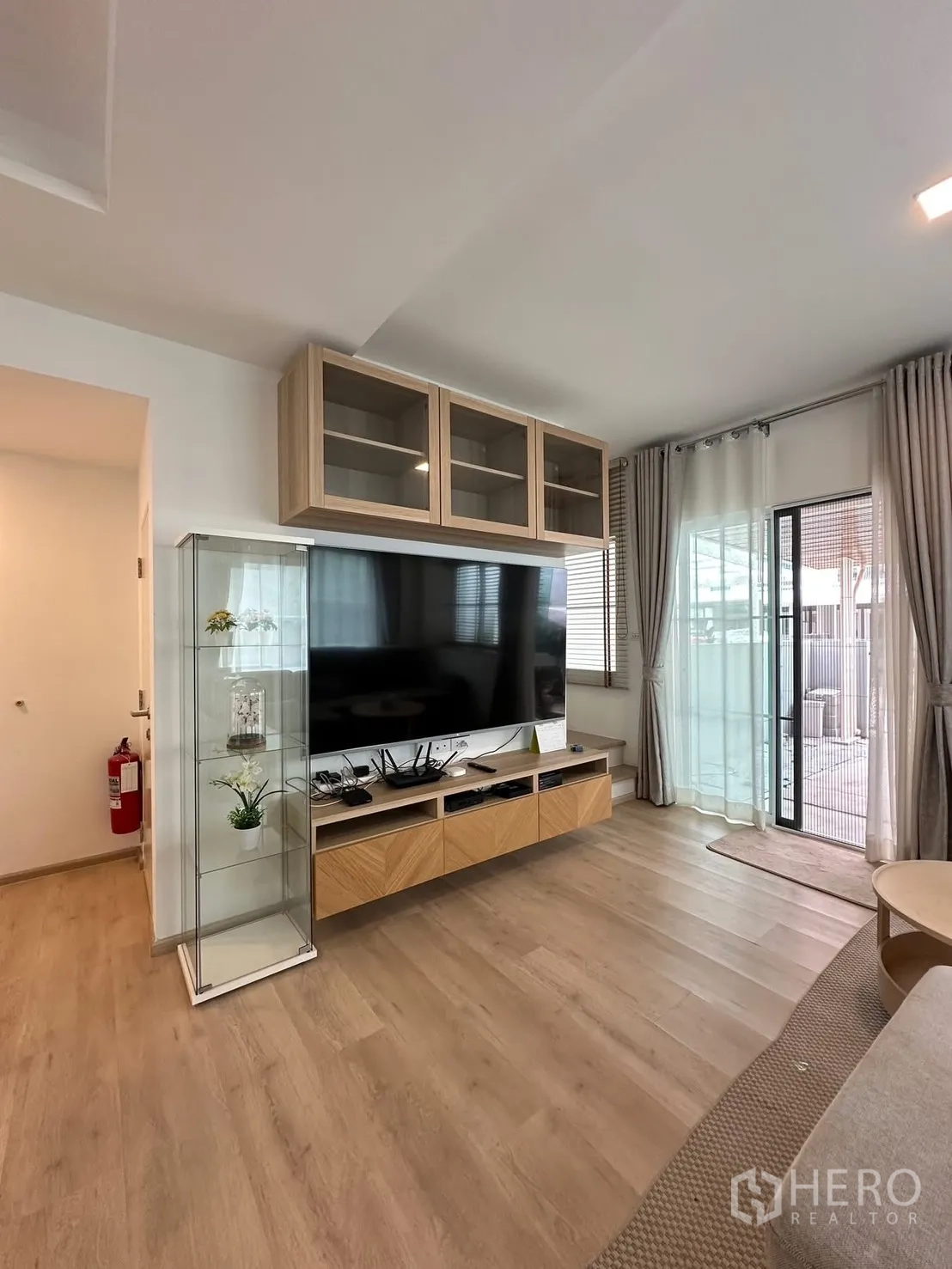 联排别墅 for rent in Prawet, Bangkok - 客厅设大型电视柜、玻璃展示柜与通向庭院的推拉门。