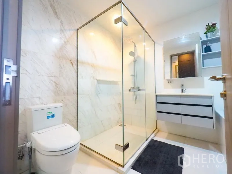 公寓 出租在Watthana, Bangkok - 浴室设玻璃淋浴间、洗手台与大理石纹墙面。