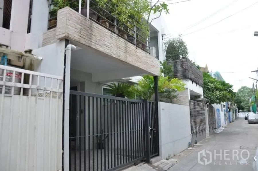 Townhouse for rent or sale in Watthana, Bangkok - Townhouse exterior in Ekkamai with secure gate, covered carport and balcony planters on a quiet lane.