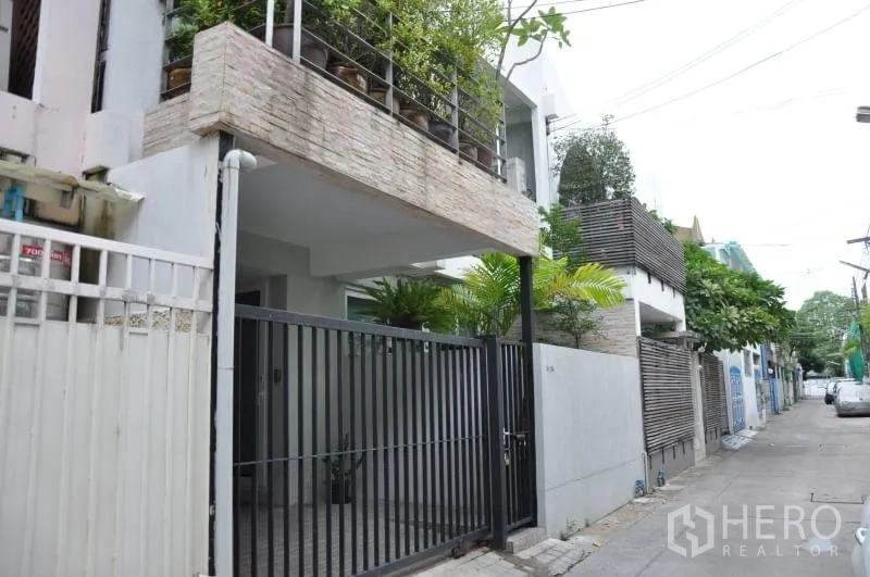Townhouse for rent or sale in Watthana, Bangkok - Townhouse exterior in Ekkamai with secure gate, covered carport and balcony planters on a quiet lane.