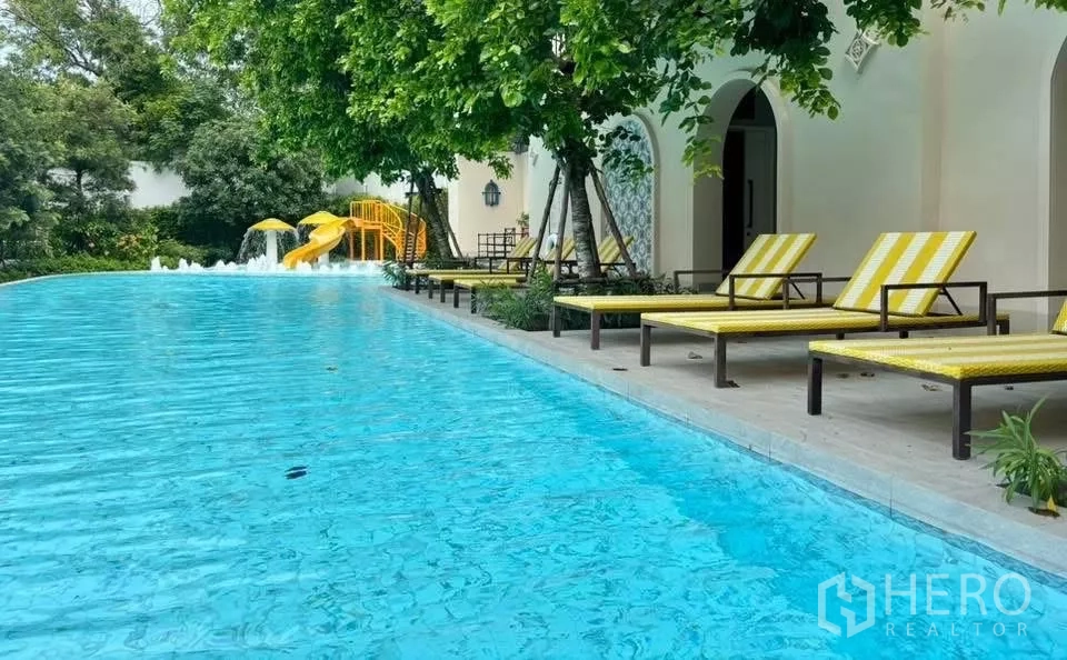 บ้าน ให้เช่าในLat Krabang, Bangkok - สระว่ายน้ำส่วนกลาง พร้อมเตียงอาบแดด ร่มเงาต้นไม้ และสไลเดอร์เด็ก