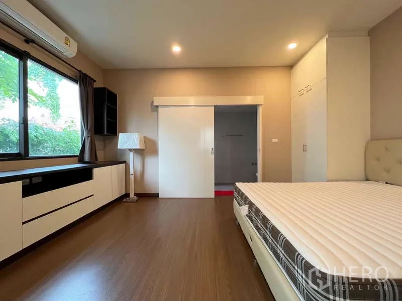 Detached House for sale in Prawet, Bangkok - Spacious bedroom with built-in wardrobes, large window, and sliding door to an ensuite bathroom.