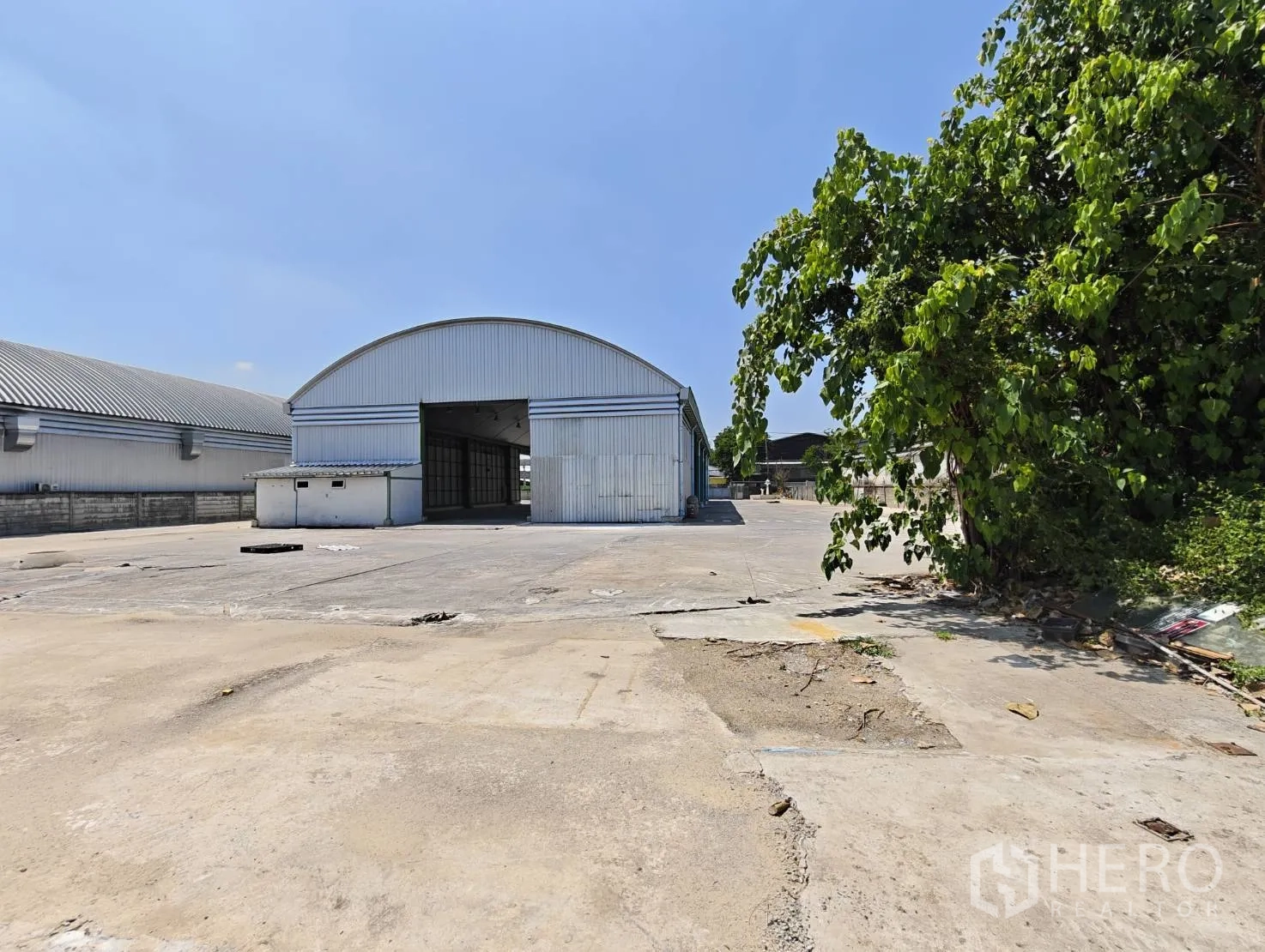 仓库 for rent in Lak Si, Bangkok - 仓库正面，滑动工业大门与宽大的前场，旁有树木。