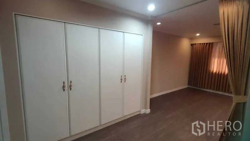 Home Office for rent in Watthana, Bangkok - Bedroom with built-in closet, warm lighting and floor-length curtains.