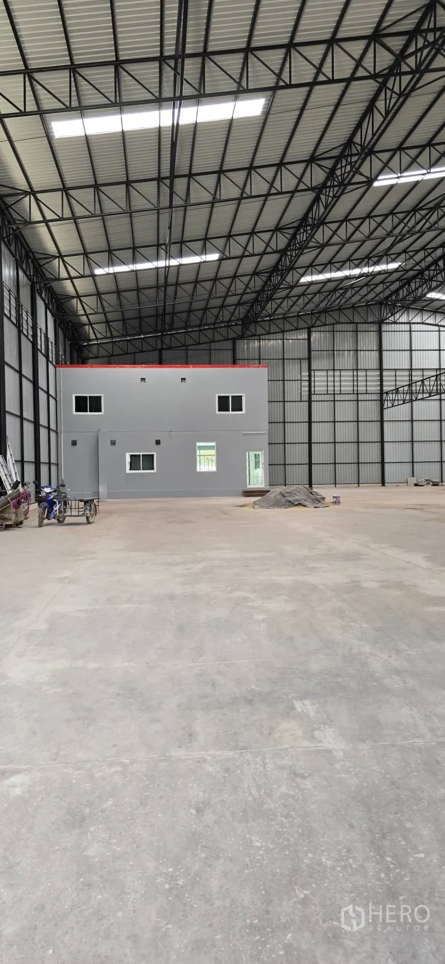 Factory for rent in Mueang Samut Sakhon, Samut Sakhon - Vast warehouse interior with high steel truss roof, concrete floor, and a two-storey gray office block at the rear.