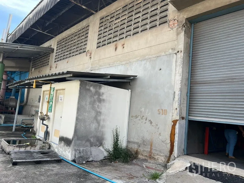 Warehouse for rent in Mueang Samut Prakan, Samut Prakan - Warehouse exterior service area featuring a roller shutter loading door, utility room and piping.