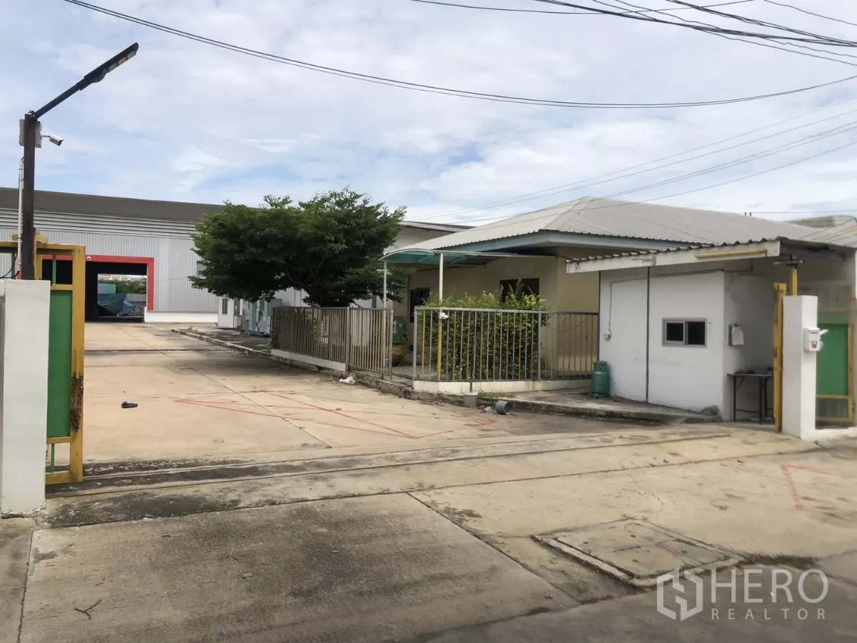 Factory for rent in Mueang Samut Prakan, Samut Prakan - Entry gate with tree-lined yard and view of metal factory warehouse