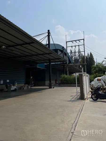 货栈 出租在Si Racha, Chon Buri - 仓库侧视图，宽阔混凝土场地与雨棚及供电设施