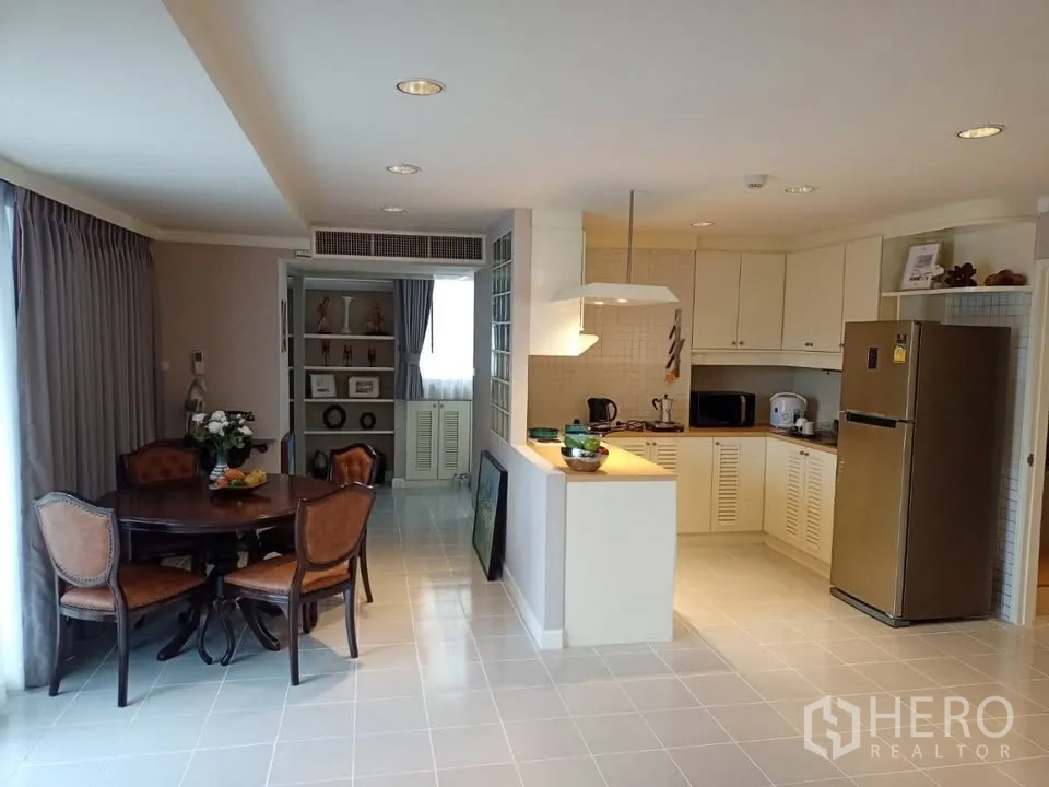 Condominium for rent in Watthana, Bangkok - Open-plan kitchen with white cabinets, dining table, and full-size refrigerator.