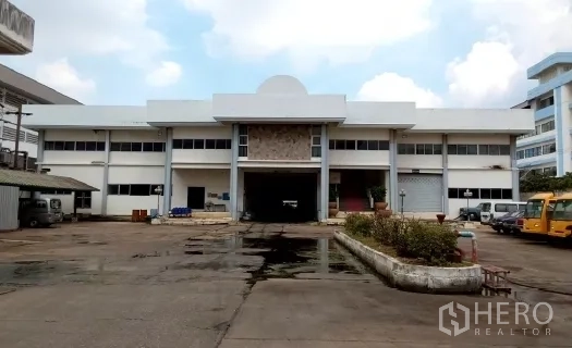 โรงงาน ขายในBang Phli, Samut Prakan - ด้านหน้าโรงงานสูงสองชั้นพร้อมทางโหลดสินค้าคลุมหลังคาและลานกว้าง.