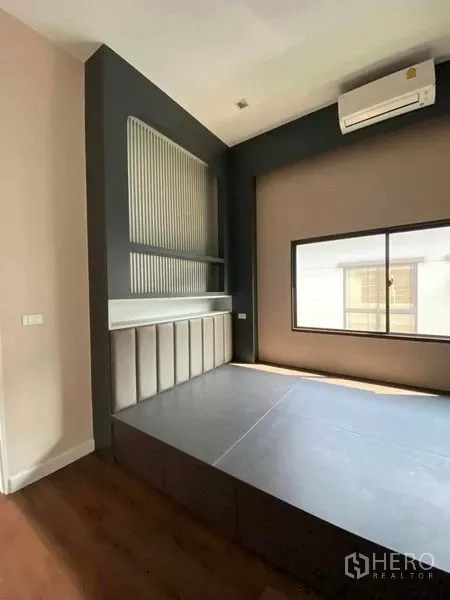 Detached House for sale in Don Mueang, Bangkok - Bedroom with raised platform bed, paneled accent wall, window and wood flooring.