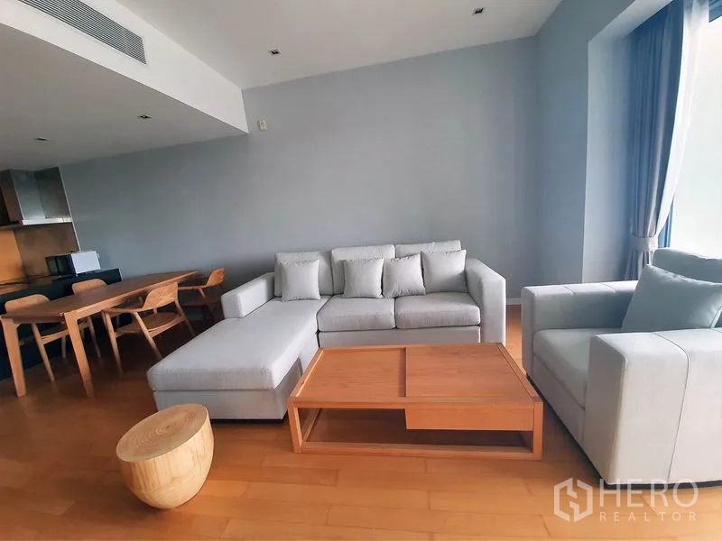 Condominium for rent in Yan Nawa, Bangkok - Open-plan living and dining area with sofa set, wooden table and large window.